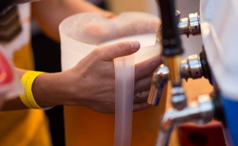 A close up of a beer pitcher while a volunteer is filling the pitcher. The pitcher is almost filled to the brim. The hand has a yellow wristband on it.