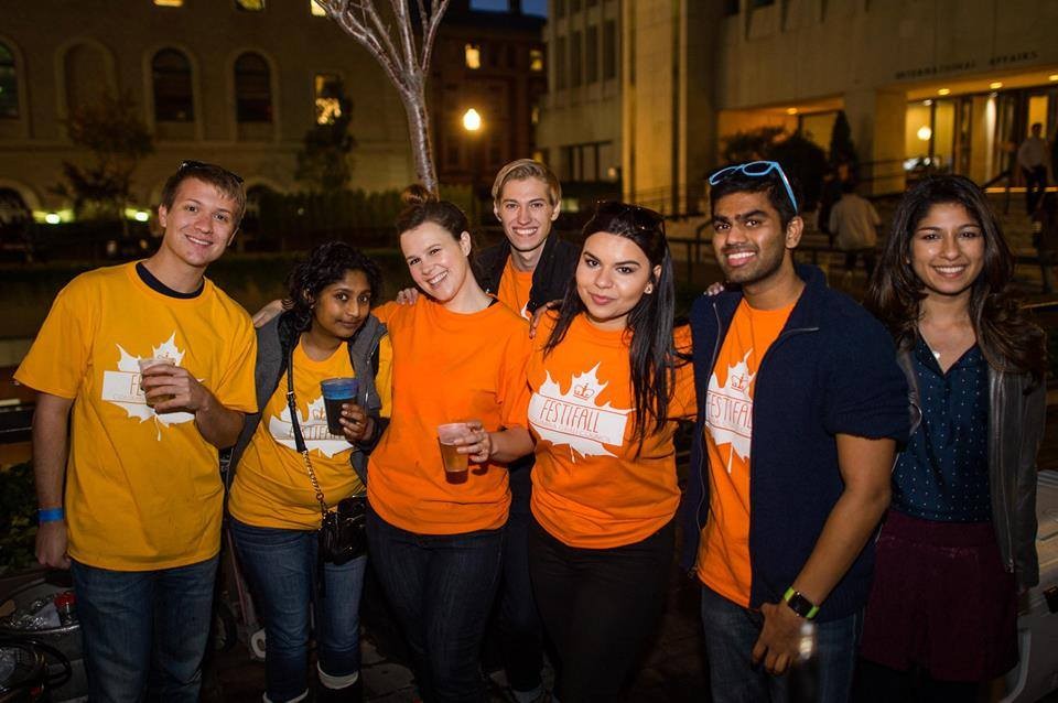 7 Volunteers posing for a group shot at FestiFall 2015. 3 students are holding liquid filled cups while others are posing with their arms around each other.